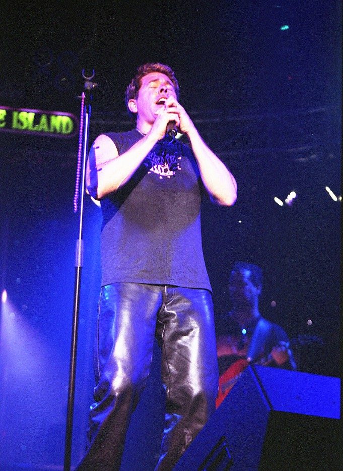 Tim McGeary singing into a microphone under purple stage lights